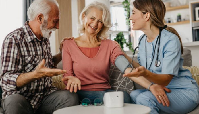 1440464714-612×612 Senior couple consulting health and medical report with a doctor at home. Old man and elderly woman visiting the nurse, and checking blood pressure.